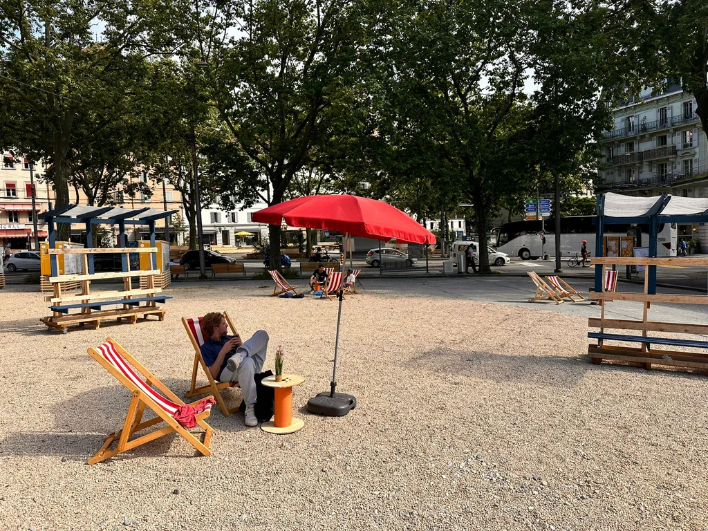 Aménagement éphémère d’Îlot Tunnel : transats, parasols et structures en bois sur la place